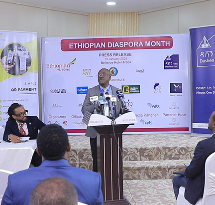 A speaker stands at a podium addressing an audience during Ethiopian Diaspora Month. The backdrop features sponsor logos and event details including Ethiopian Diaspora Month, press release, and Bellevue Hotel and Spa. The setting is a formal conference room with seated attendees and a professional, collaborative atmosphere.